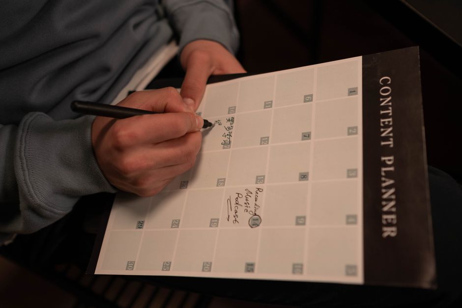Persona che scrive su un calendario mensile intitolato 'Content Planner' con una penna, pianificando contenuti.