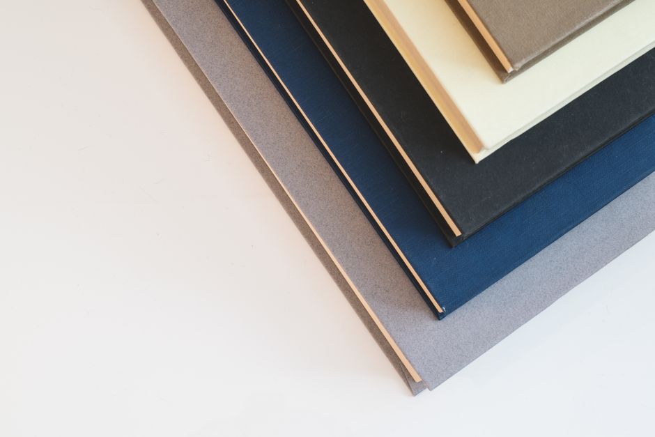Stack of hardcover books with plain, minimalistic covers in neutral colors arranged on a light surface.