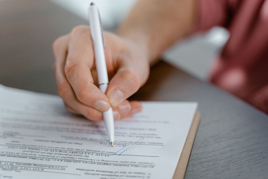 Mano che firma un contratto su un tavolo grigio con una penna bianca.